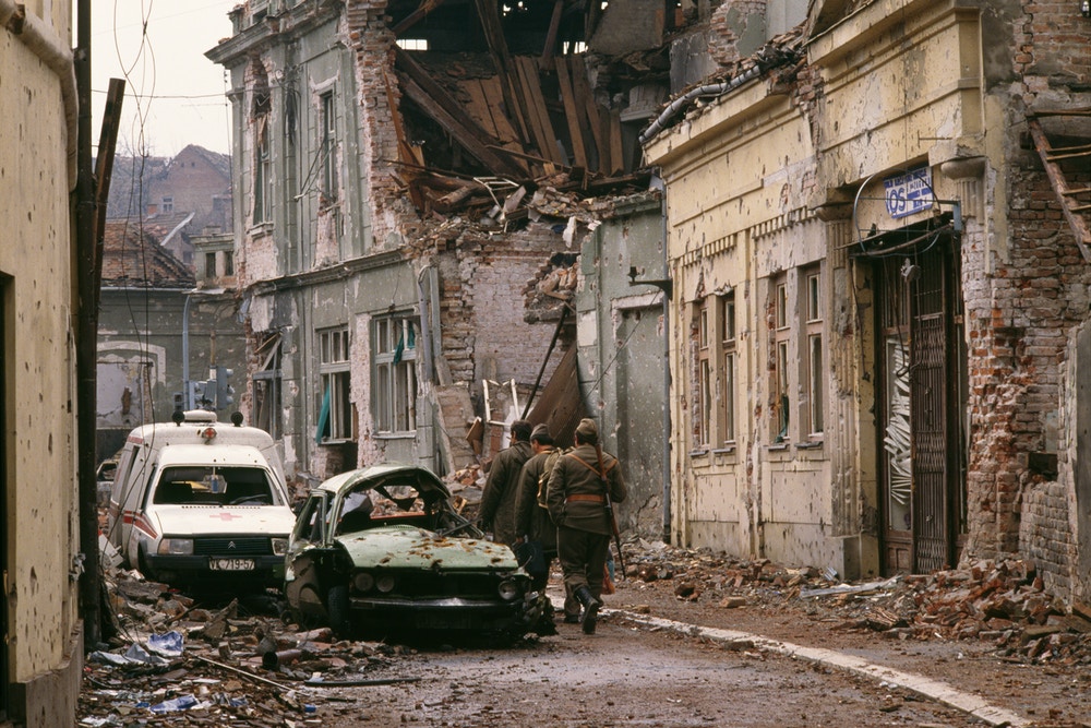 Yugoslavian soldiers and Serb paramilitaries, including Zeljko "Arkan" Raznatovic, walk past bombed buildings riddled with bullet holes and streets filled with rubble after a three-month battle between the Croatian armed forces and the Yugoslavian Federal Army in Vukovar. The Yugoslavian Federal Army completely destroyed the Croatian city, killing thousands of civilians, while the Serbian Volunteer Guard, formed by Raznatovic, was responsible for massive ethnic cleansing campaigns against Bosnian Croats. (Photo by Antoine GYORI/Sygma via Getty Images)