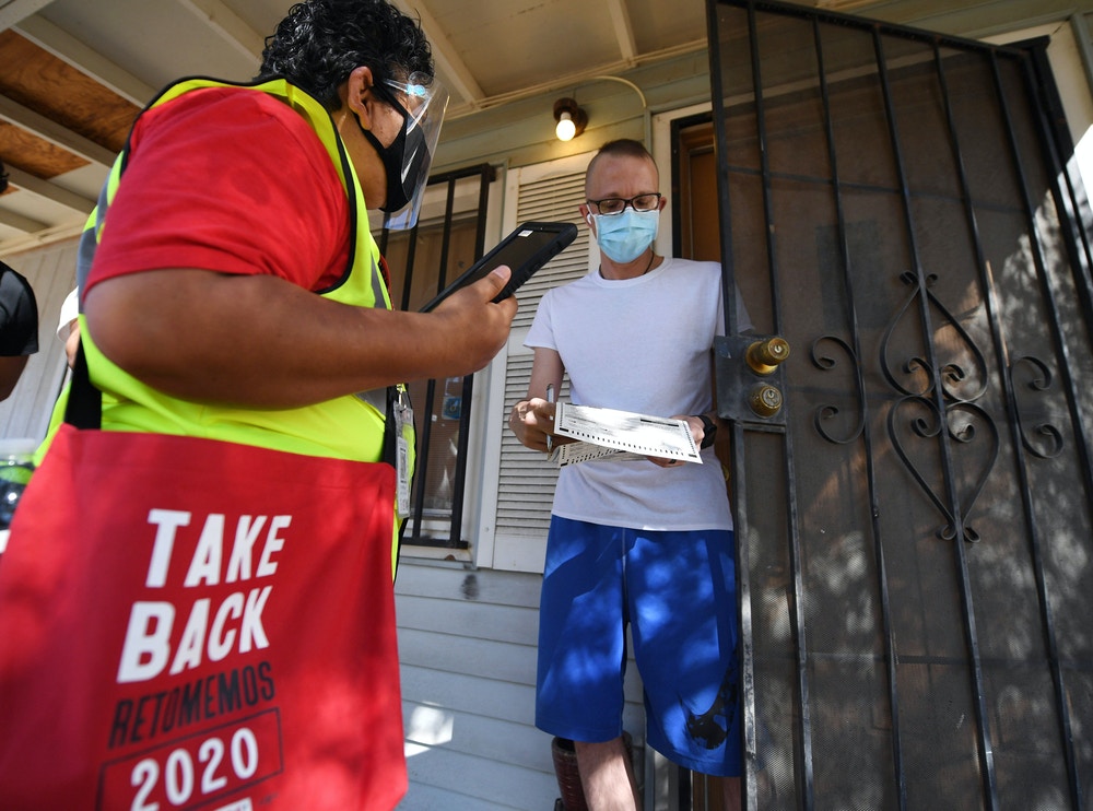 Democratic party activist Iris Acosta (R) talks to Phoenix resident Christopher Lowe as he completes form, as Acosta canvasses the suburbs of Phoenix, Arizona, October 15, 2020 ahead of the US presidential election. - After losing her housekeeping job at a California hotel, Iris Acosta grabbed her most comfortable pair of walking shoes and headed to Arizona to drum up support for Joe Biden. Acosta is part of a small army of union workers who have rushed to Arizona -- a battleground state won by Donald Trump in 2016 but considered a toss-up this time around -- in the hope of tilting the vote in favor of the veteran Democrat. (Photo by Robyn Beck / AFP) (Photo by ROBYN BECK/AFP via Getty Images)